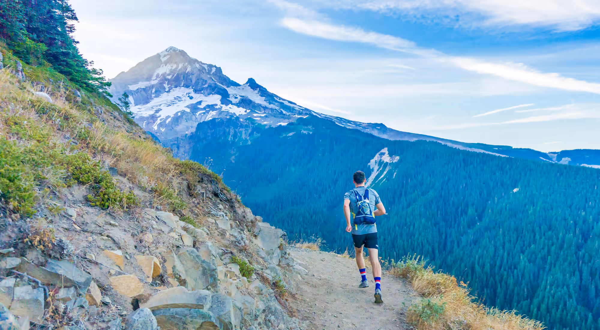 A runner on a ridge trail, a snow-covered mountain range in the distance.