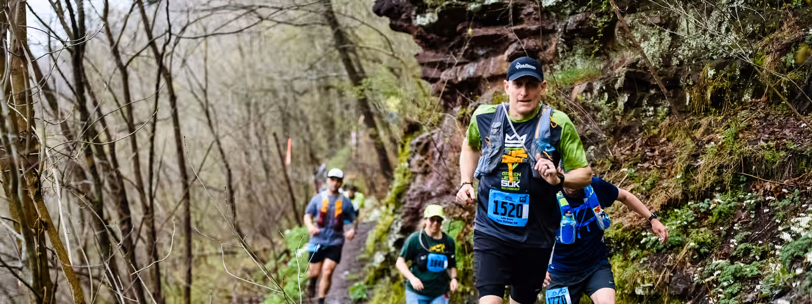 A group of race-numbered runners on a wet, rocky climb.